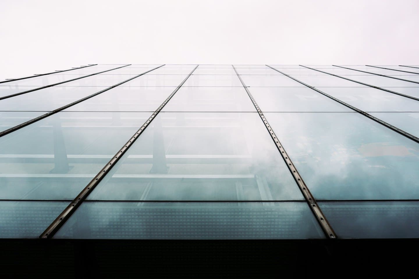Modern glass building facade with reflective panels and metal strips.